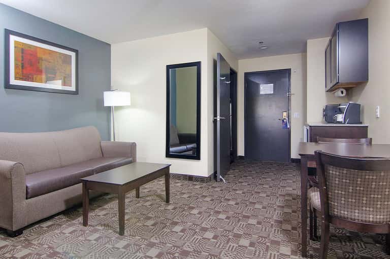 Hotel suite interior with sofa, coffee table, kitchenette, and neutral color scheme
