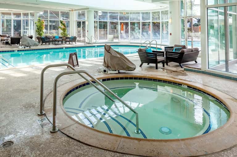 Indoor pool facility with spa hot tub, loungers, and large window walls