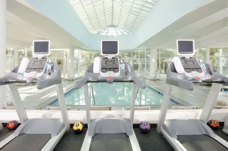 Gym interior with three treadmills overlooking an indoor swimming pool