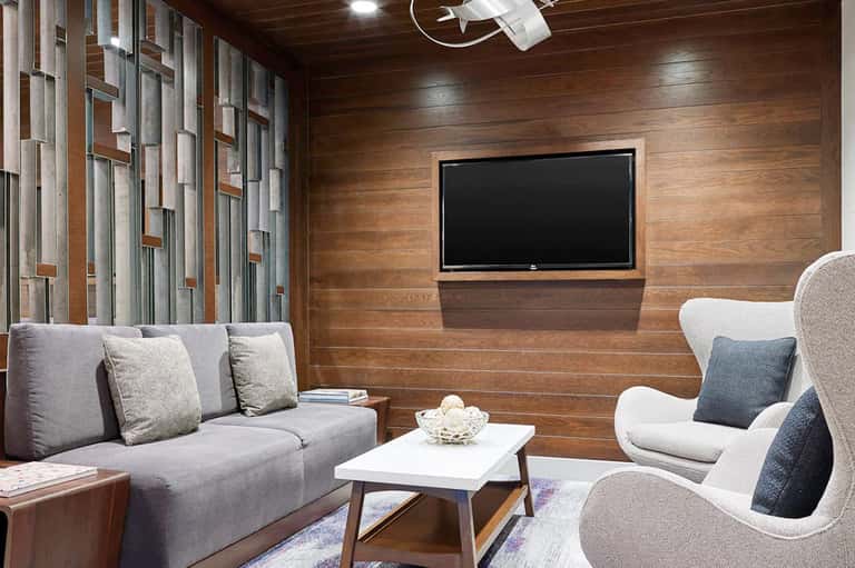 Modern home theater room with wood paneling, gray sofa, and mounted flat-screen TV