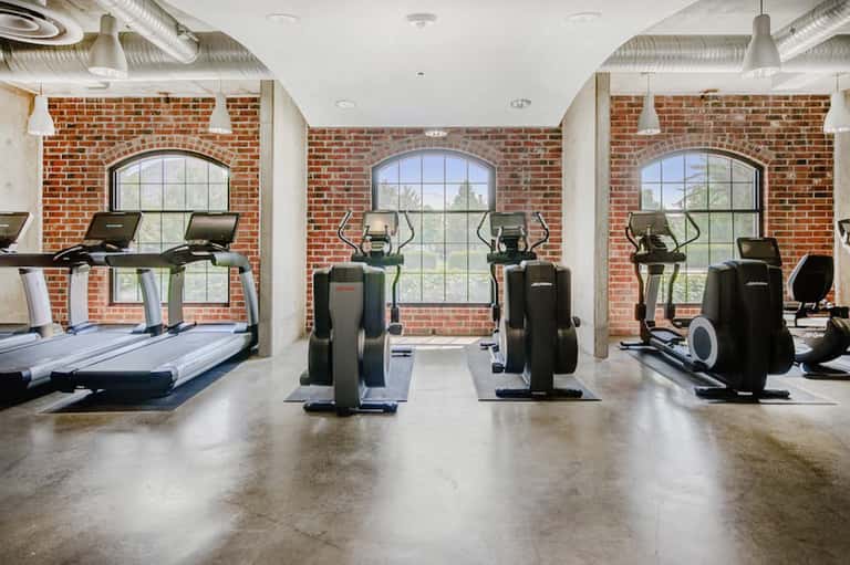 Fitness center with treadmills, ellipticals, and exercise equipment facing exposed brick walls