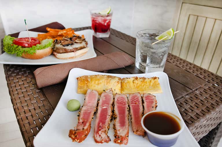 Dining table with seared tuna slices, grilled fish with pineapple, and tropical drinks