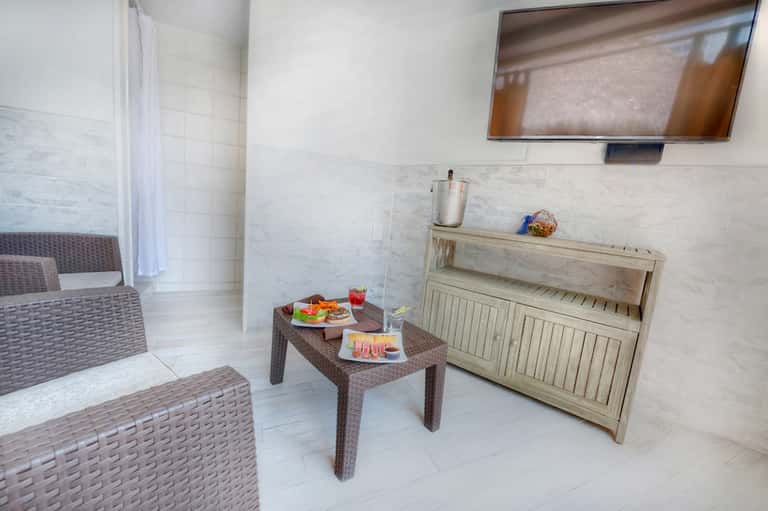 Modern spa relaxation room with wicker seating, small table with snacks and drinks, and TV