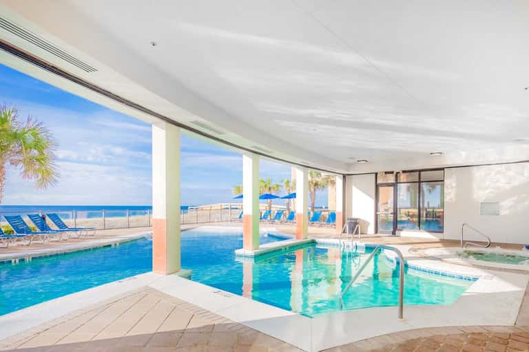 Indoor pool and hot tub facility with ocean view through large windows and beach beyond
