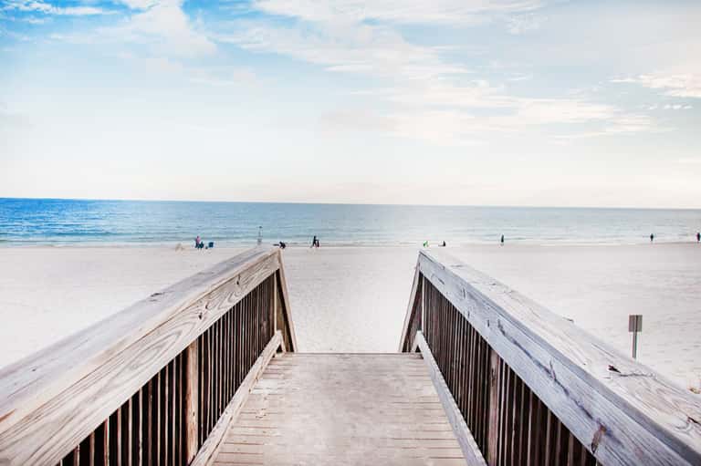 Wooden boardwalk or beach access ramp leading to sandy beach with ocean and swimmers in background