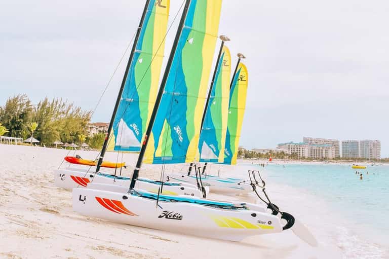 Colorful sailboats with blue, yellow and green sails lined up on sandy beach