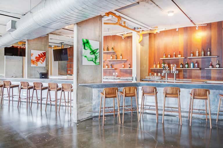 Contemporary bar interior with wooden seating, concrete walls, extensive bottle display, and industrial design elements
