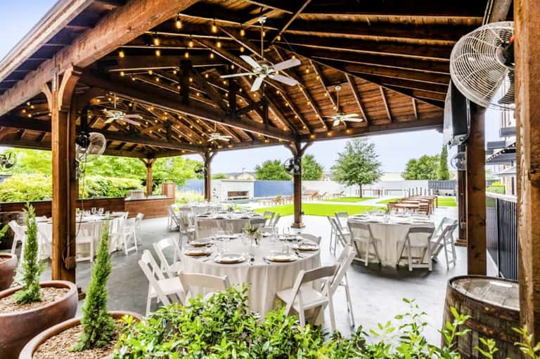 Wooden pavilion event space with rustic beams, string lights, round tables with white linens and green lawn