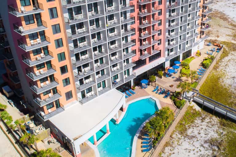 Aerial view of beachfront resort with colorful buildings, pool, and sandy beach access