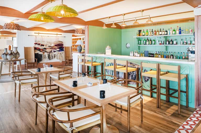 Modern restaurant interior with mint green walls, wooden furniture, brass pendant lights, and full bar