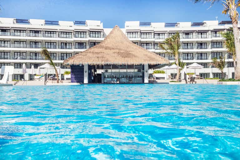 Resort swimming pool with thatched roof bar and white modern hotel building backdrop