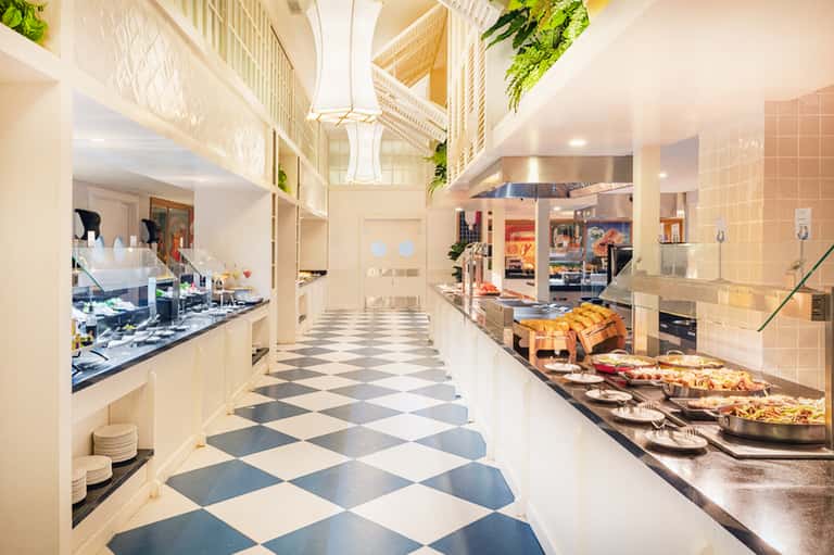 Elegant food service corridor with checkered flooring, multiple food stations, and hanging plants