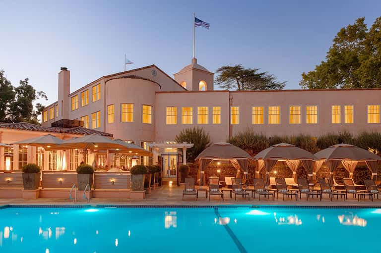 Upscale resort pool at dusk with illuminated building, umbrellas, and lounge seating
