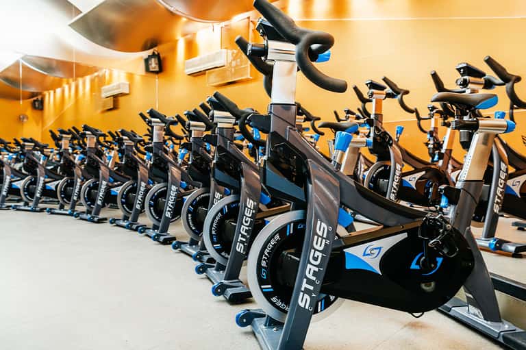 Modern fitness center with rows of black and blue stationary bikes under yellow ceiling