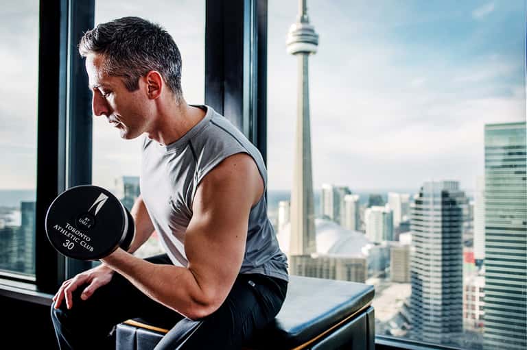 Man exercising with dumbbell in high-rise gym with city and CN Tower views