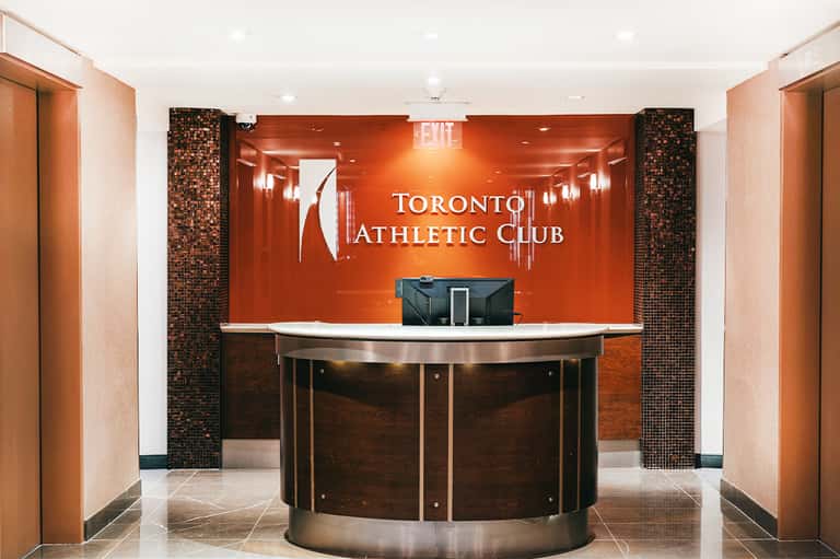 Toronto Athletic Club reception desk with orange accent wall and brick columns