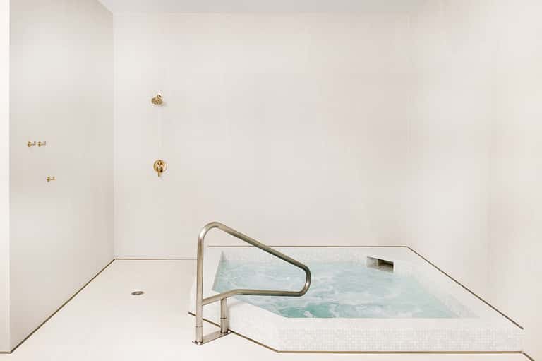Modern spa hot tub with white tile and metal handrail in minimalist bathroom