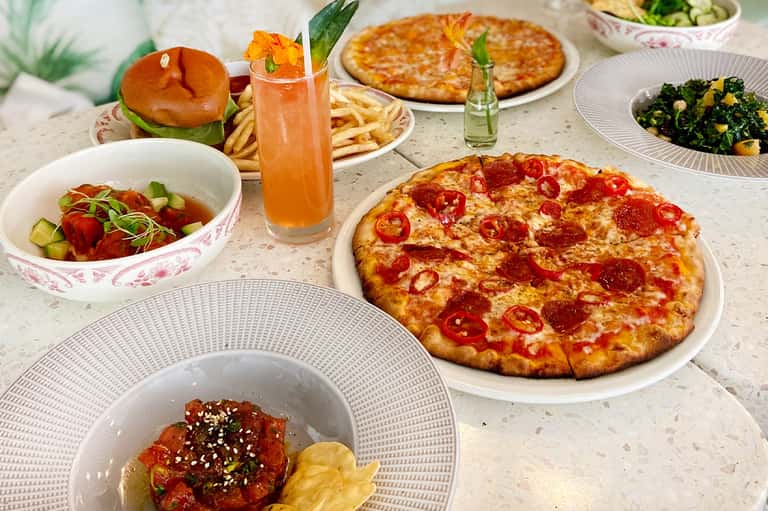 Casual dining table with pizza, burger, fries, salad, and peach-colored beverage