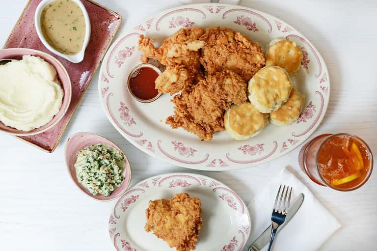 Southern comfort food plating with fried chicken, biscuits, coleslaw, and mashed potatoes on decorative plates