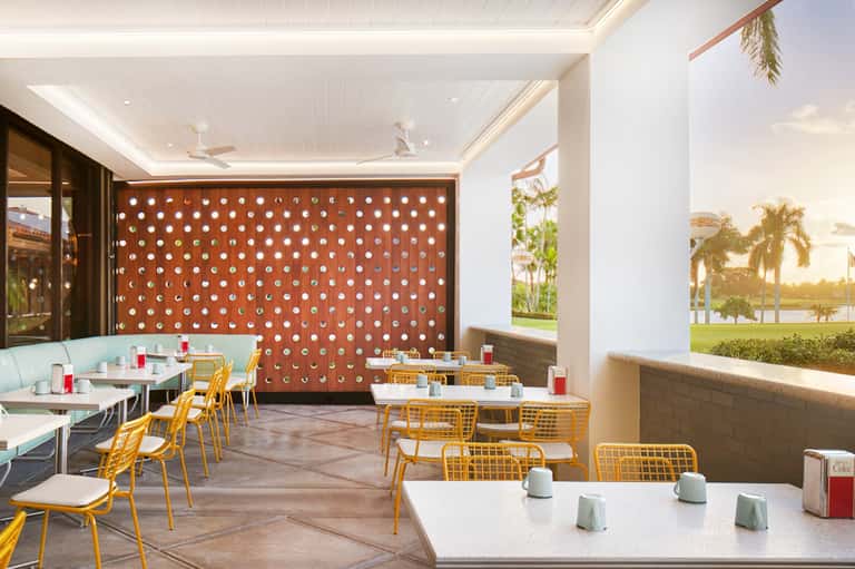 Modern casual dining space with yellow chairs, geometric wall pattern, and panoramic waterfront windows