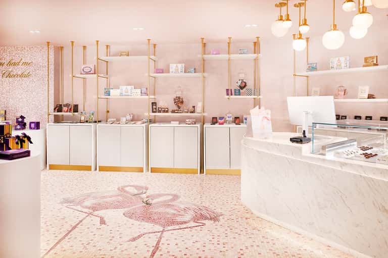 Luxury pink retail boutique interior with gold shelving, marble counter, and decorative display items