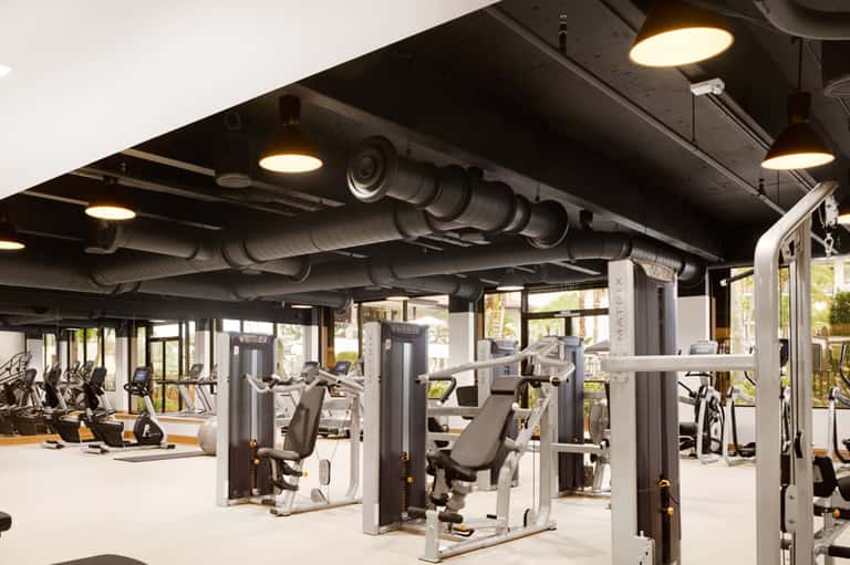 Modern gym with exercise equipment, exposed ceiling pipes, and natural lighting from windows