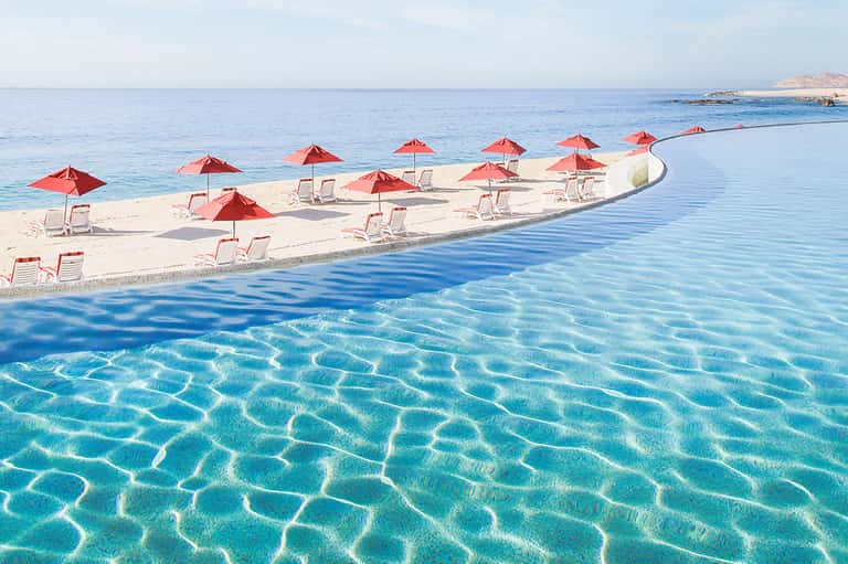 Beach scene with red umbrellas, white loungers, and crystal-clear turquoise water