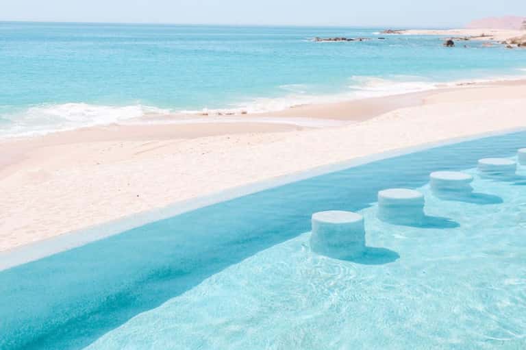 Pristine turquoise lagoon with white sand beach, clear shallow water, and distant rocky coastline