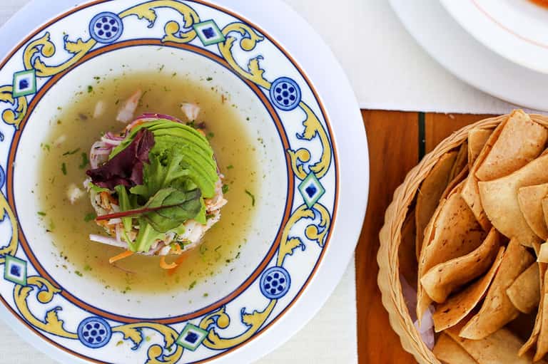 Gourmet soup bowl with decorative blue and yellow rim, fresh greens, and crispy tortilla chips