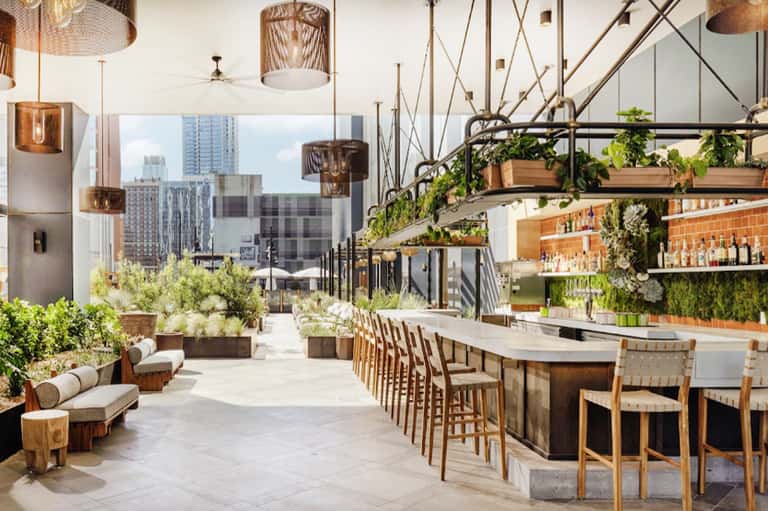 Rooftop bar and dining area with hanging copper lights, greenery, and city skyline views