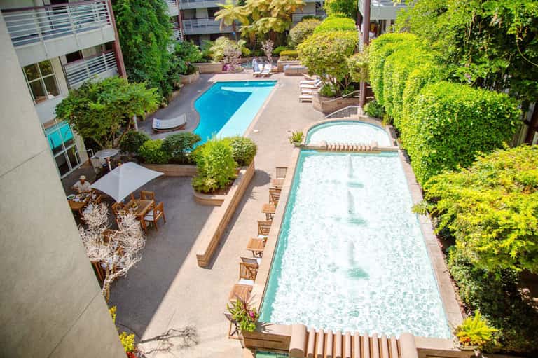 Overhead view of resort courtyard with two lap pools, hot tub, lush greenery, and multi-story building