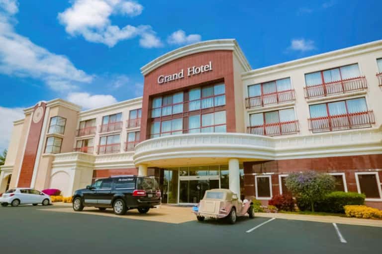 Grand Hotel exterior with red brick and cream-colored facade, parked cars, and landscaping