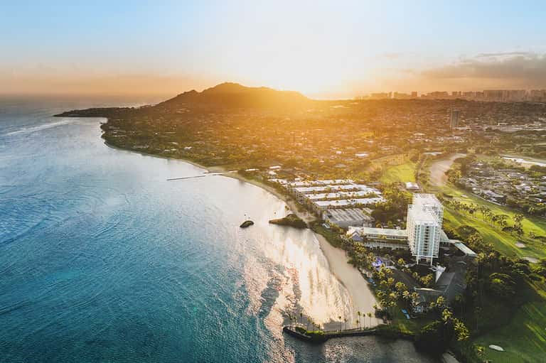 Aerial view of sandy beach cove with white resort buildings surrounded by green hillside