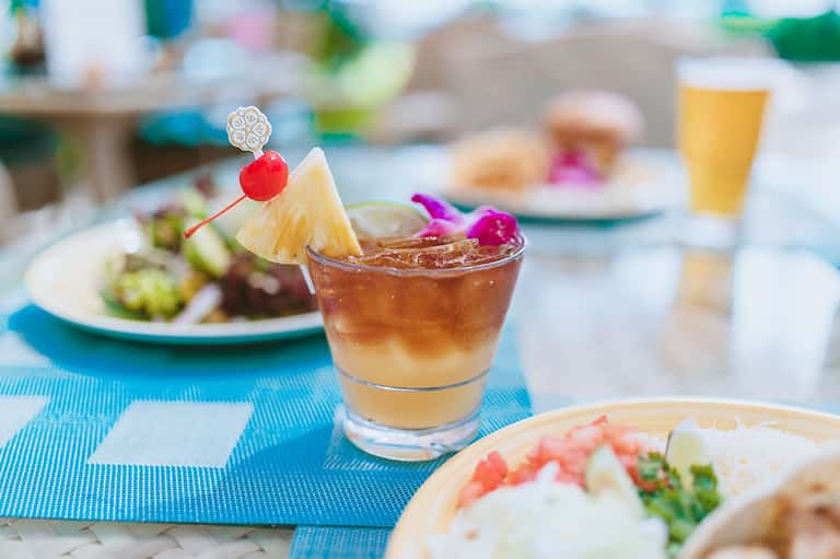 Tropical cocktail with pineapple garnish and appetizers on blue tablecloth