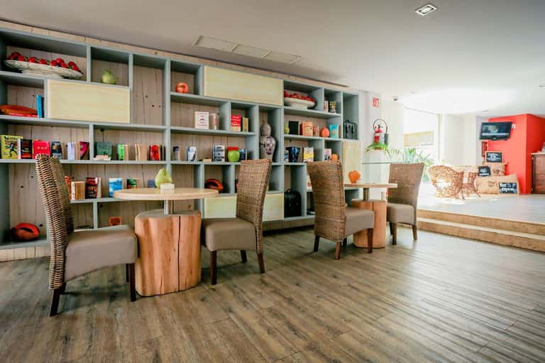 Modern hotel lobby with wooden shelving, wicker chairs, wood tables, and contemporary décor