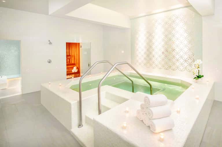 Spa hot tub with green water and rolled white towels, sauna door visible in background