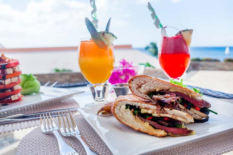 Colorful tropical cocktails and fish tacos with lime garnish served beachside with ocean view