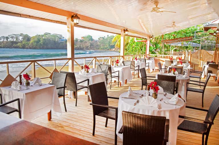 Beachfront dining terrace with white tablecloths, ocean views, and wooden deck overlooking the shore