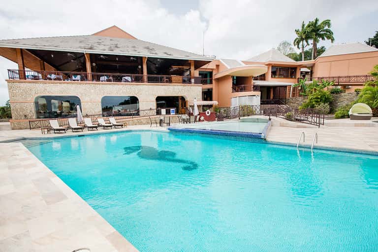 Resort pool with turquoise water, terracotta buildings, and palm trees at sunset