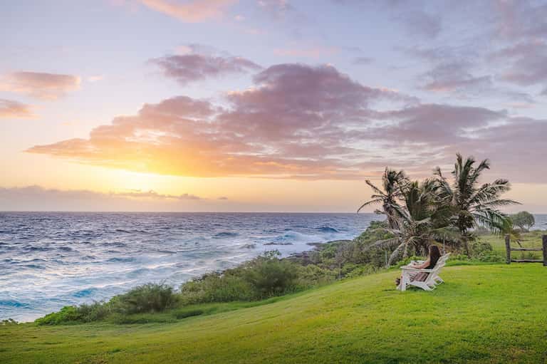 Oceanfront Adirondack chair on grassy lawn overlooking tropical coastline at golden sunset hour