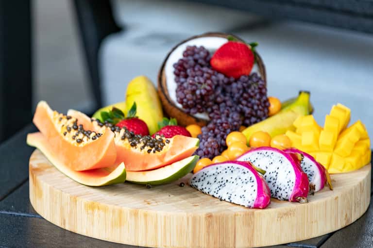 Wooden board displaying fresh tropical fruits including papaya, mango, and dragon fruit