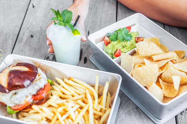 Overhead view of food and beverage spread including sandwich, fries, guacamole, chips, and mint cocktail