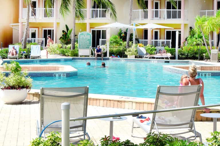 Guests swimming in bright turquoise pool with yellow umbrellas and palm-lined building