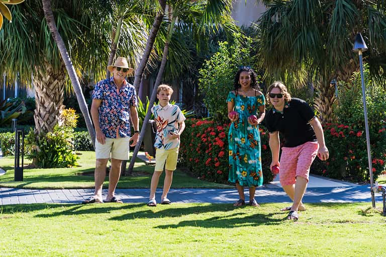 Family of five walking on sunny tropical grounds with palm trees, colorful casual clothing, and manicured green lawn