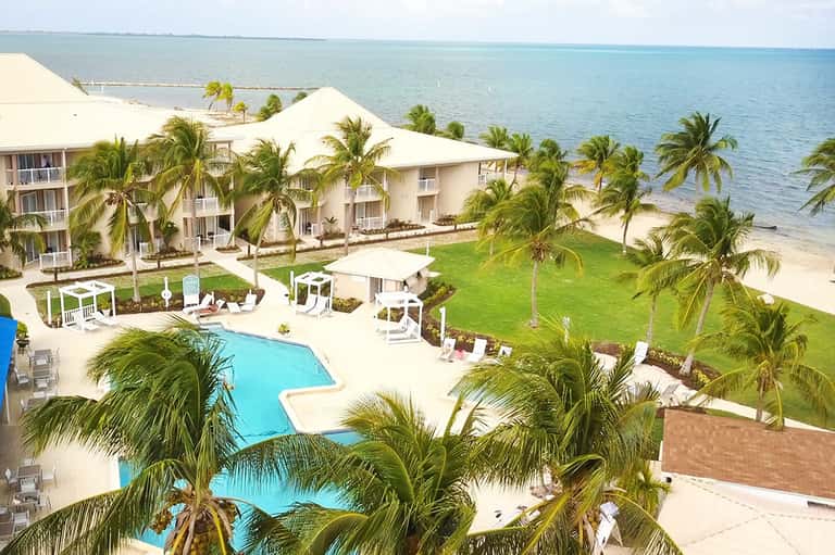 Beachfront resort with white buildings, palm trees, blue pool, and ocean view