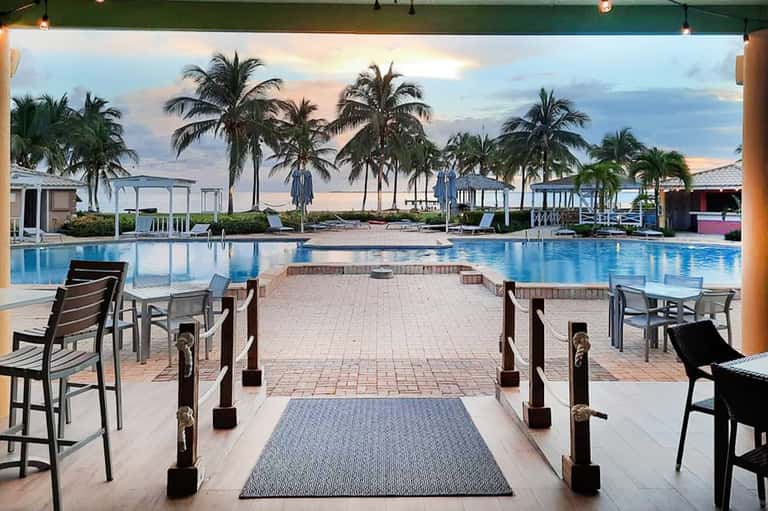 Oceanfront resort pool deck with palm trees, loungers, cabanas, and sunset water views