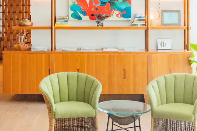 Mid-century modern lounge with wooden shelving, green armchairs, and colorful abstract artwork
