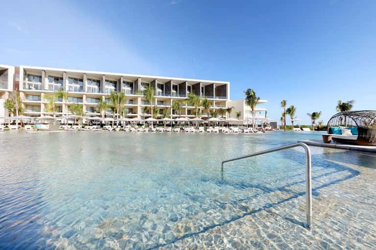 Modern luxury resort with lagoon-style pool, palm trees, white lounge chairs, and contemporary architecture