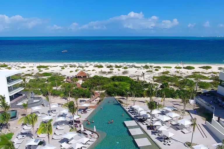 Aerial view of beachfront resort with turquoise pool, white lounge chairs, and pristine ocean
