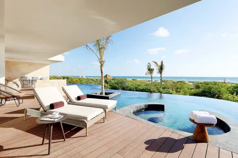 Infinity pool overlooking ocean with palm trees, modern loungers, and coastal landscape